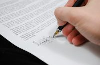 Close-up of a hand signing a legal document with a fountain pen, symbolizing signature and agreement.