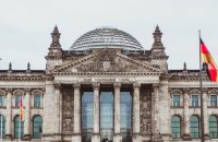 Front view of the historic Reichstag Building in Berlin, Germany, featuring prominent German flags.