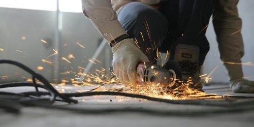 A skilled industrial worker uses a grinder creating a burst of sparks indoors.