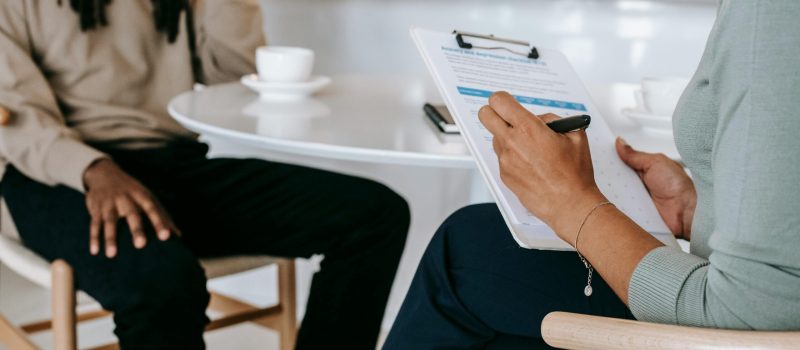 Two professionals engaged in a consultation, one taking notes on a clipboard.